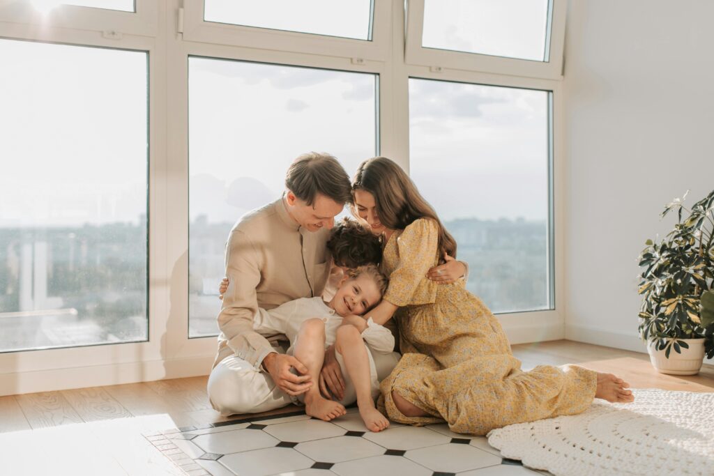 A warm family moment indoors with parents embracing their child next to a large window.