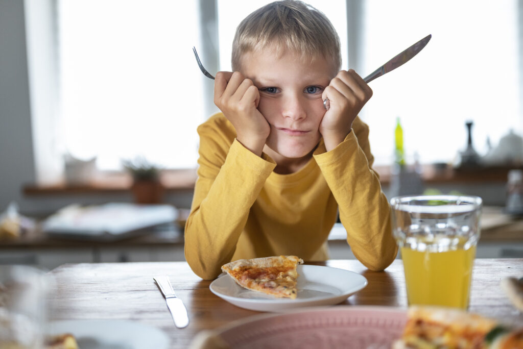 Niño con FAOD mostrando rechazo a la comida en la mesa, acompañado por sus padres.