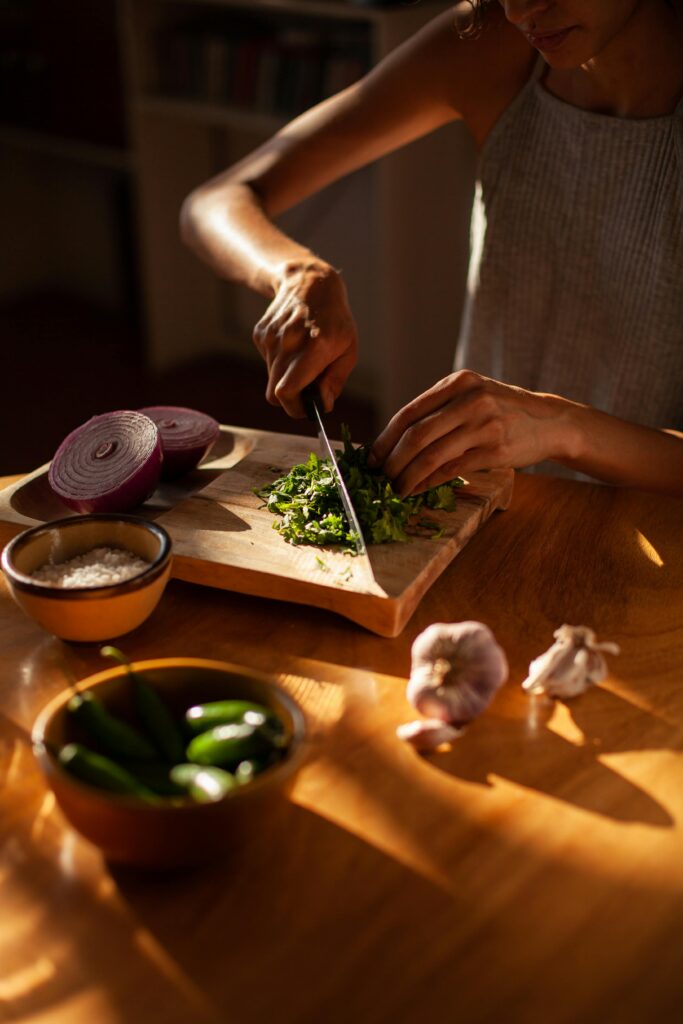 A person chopping cilantro with fresh ingredients on a wooden board in warm kitchen lighting.
